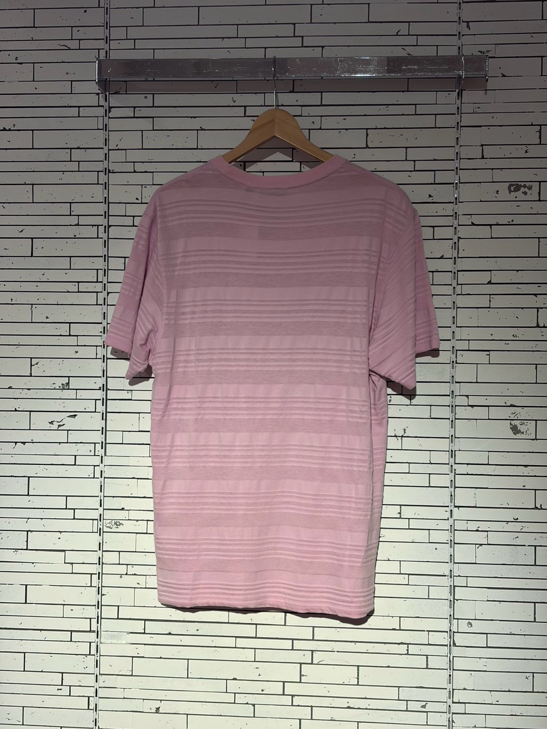 Pink short-sleeve striped T-shirt on a wooden hanger against a tiled wall display.
