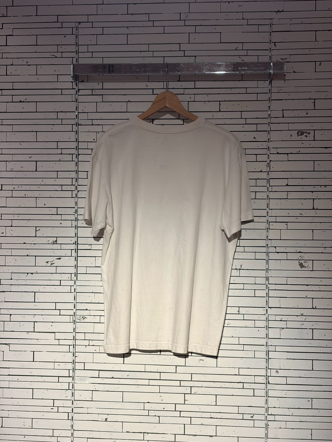 White T-shirt on a wooden hanger hanging against a white brick wall, plain and unprinted.