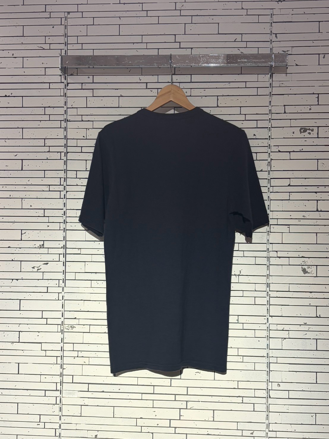Dark blue T-shirt on a wooden hanger against a light tiled wall, hanging display.