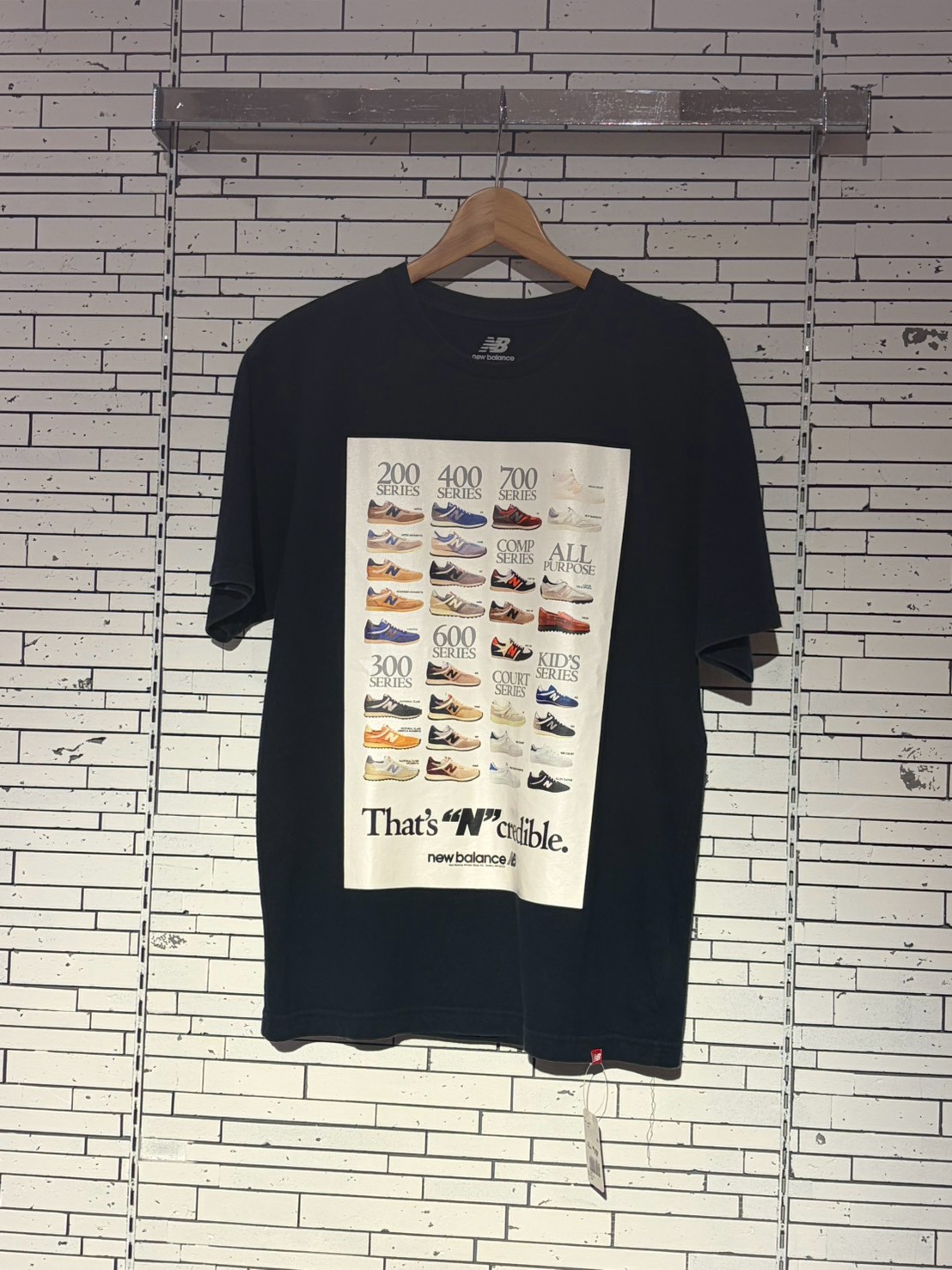 Black T-shirt on a hanger featuring a grid of New Balance sneakers and the slogan 'That's N Credible'.