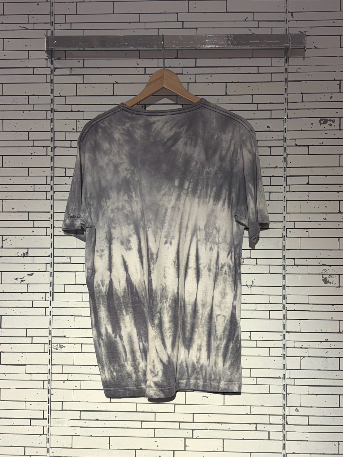 Gray tie-dye short-sleeve T-shirt on a wooden hanger against a white brick wall background.