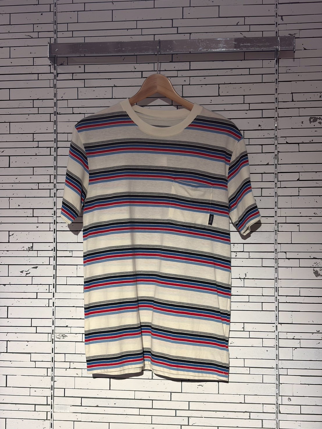 Cream crew-neck T-shirt with horizontal red, blue, and navy stripes on a wooden hanger.