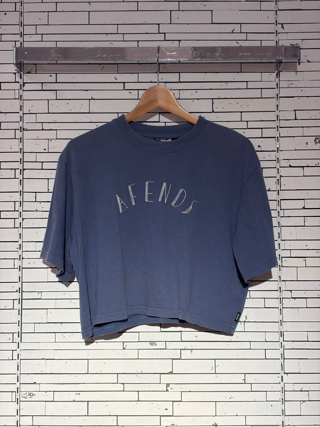 Blue oversized T-shirt on a wooden hanger, with 'AFENDS' curved logo, against a white brick wall.